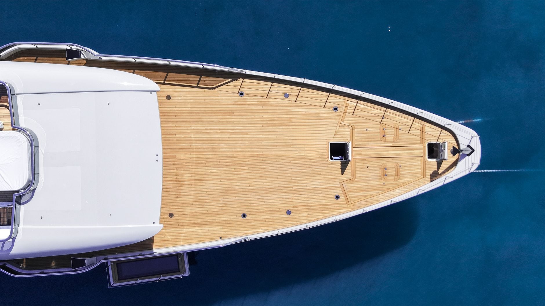 A superyacht bow from directly above — pristine teak over sapphire water