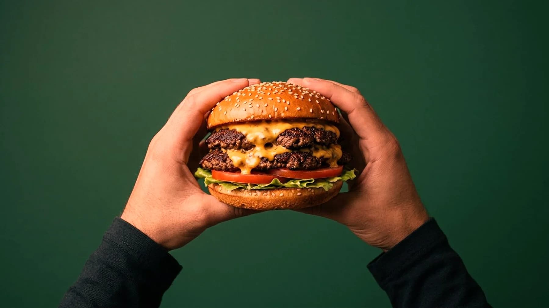 Two hands holding a double cheeseburger