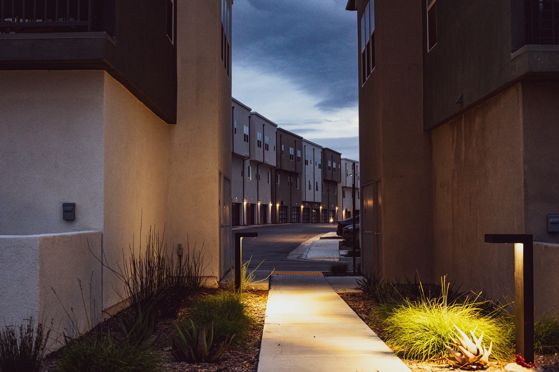 Two lit volumes at dusk sharing a bollard-lit garden path