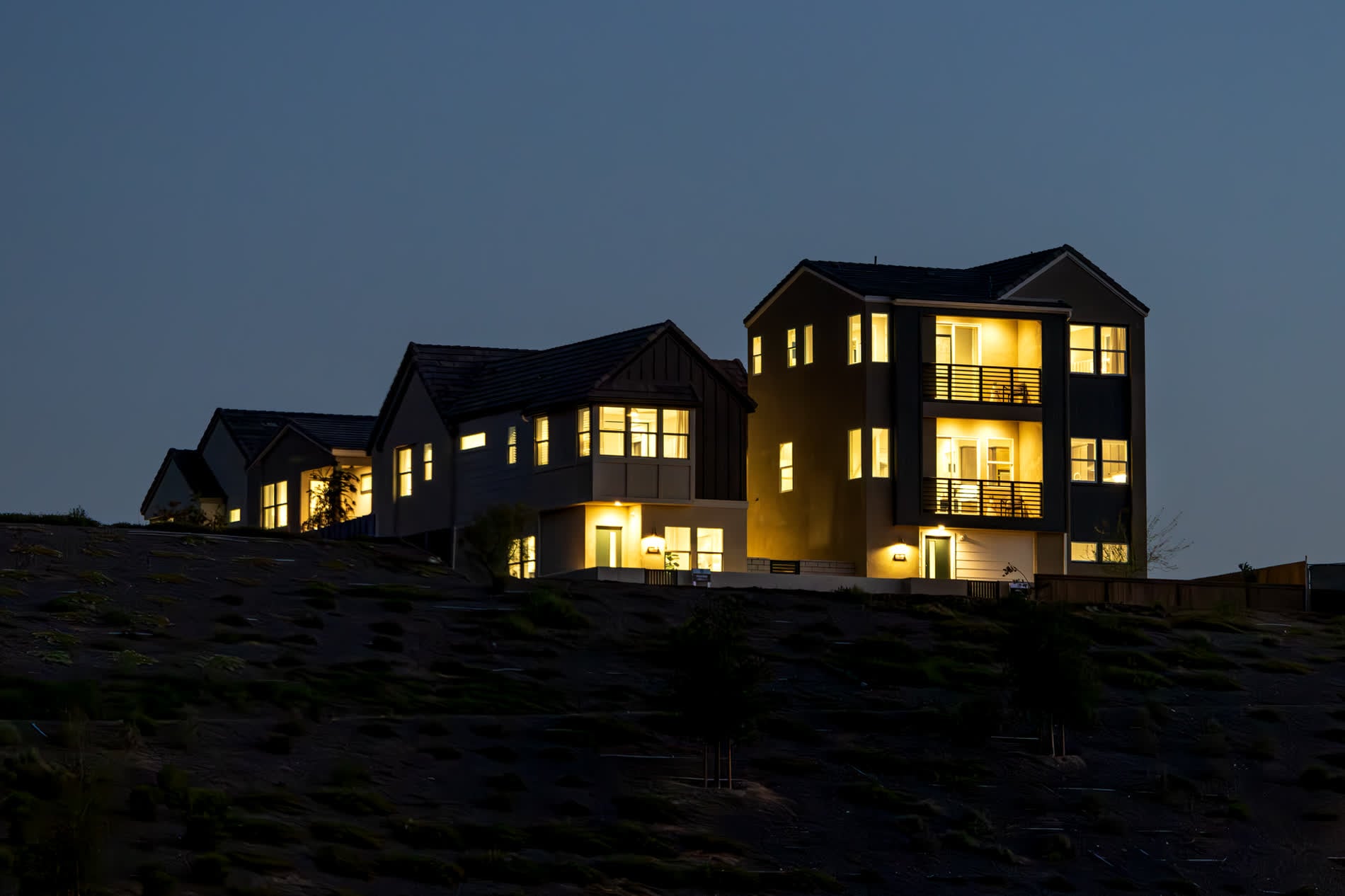 New houses standing on a raw graded hillside at dusk, bare dirt in the foreground
