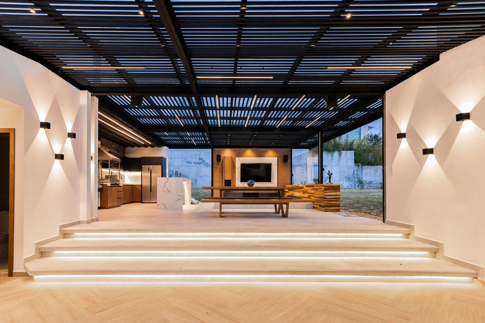 A steel-slatted outdoor room at blue hour, lit from the steps