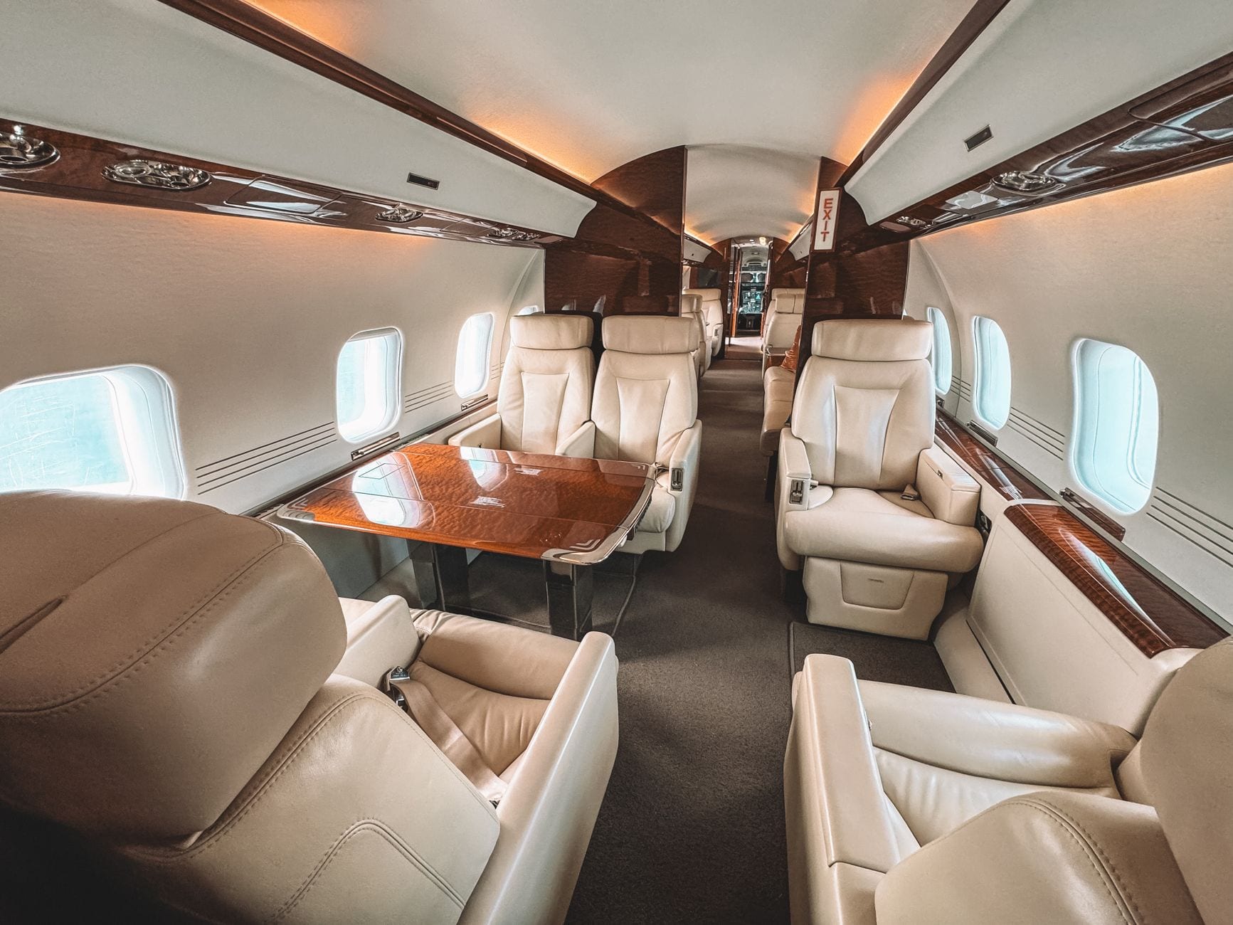 A business-jet cabin: cream leather club seats and a walnut table