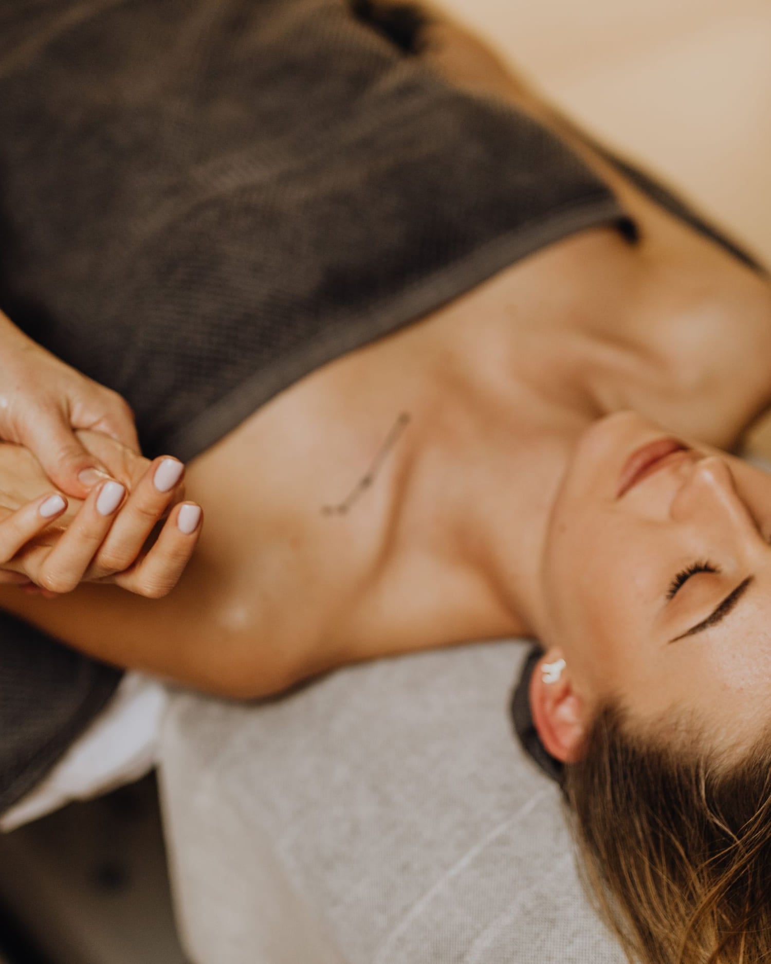 A client on a treatment couch, a practitioner's hands at her wrist