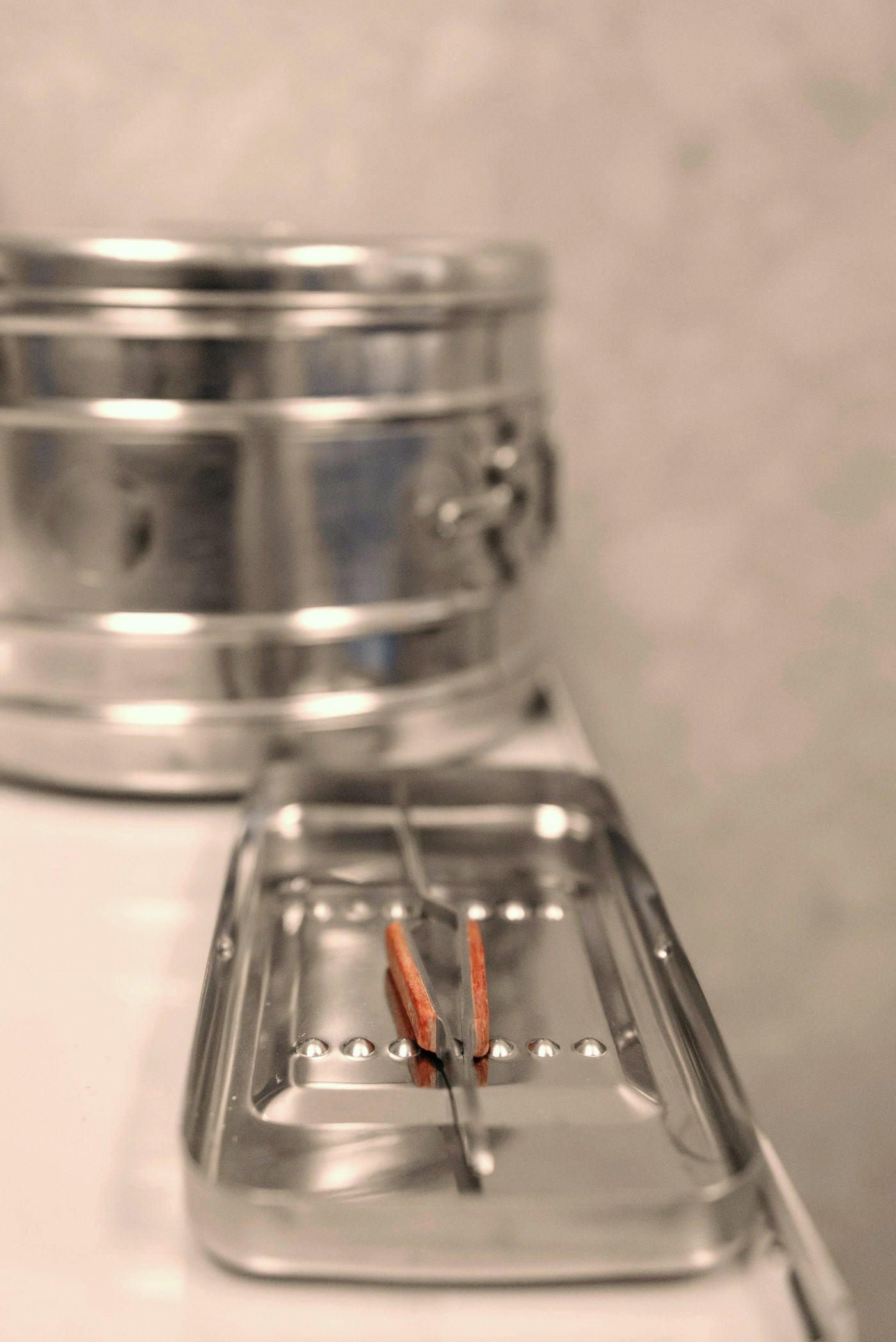 A steel instrument tray and sterilisation drum on a clean surface