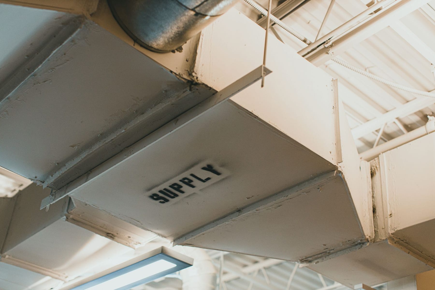 A white supply duct in an industrial ceiling