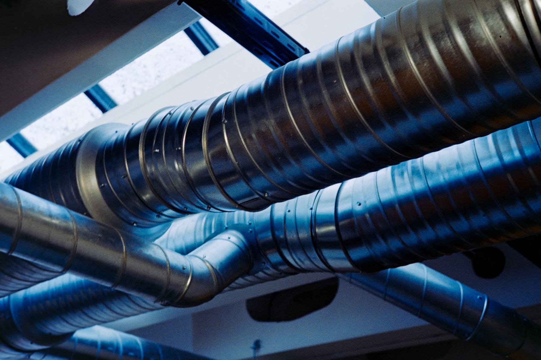Blue spiral ductwork in a mechanical room, lit from a skylight