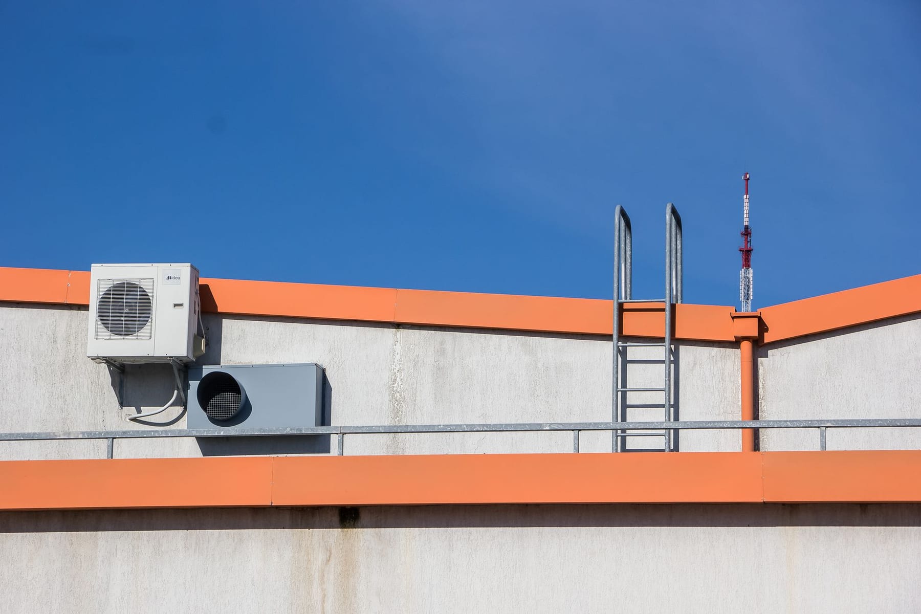 A new condensing unit on a rooftop with an orange parapet under a blue sky
