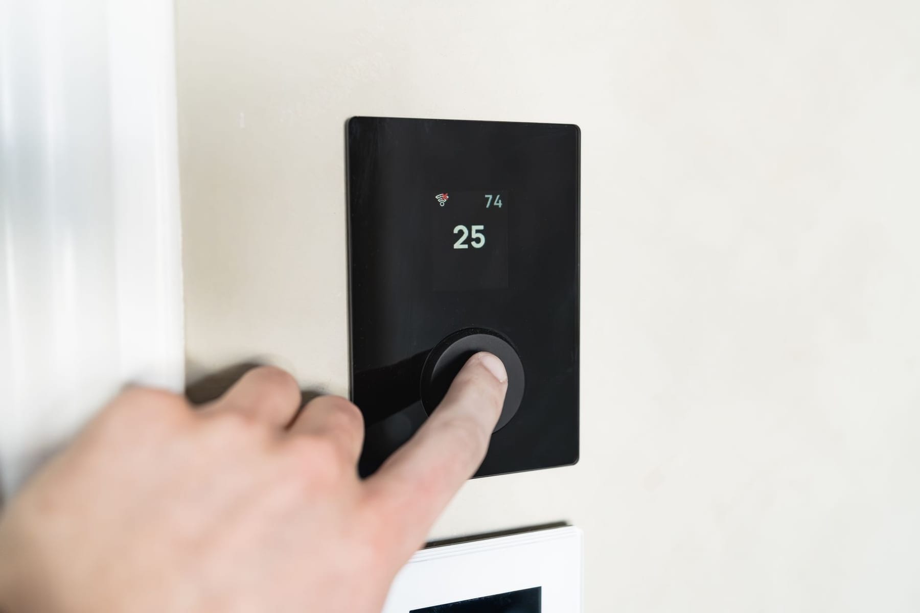 A finger on a wall thermostat reading 74