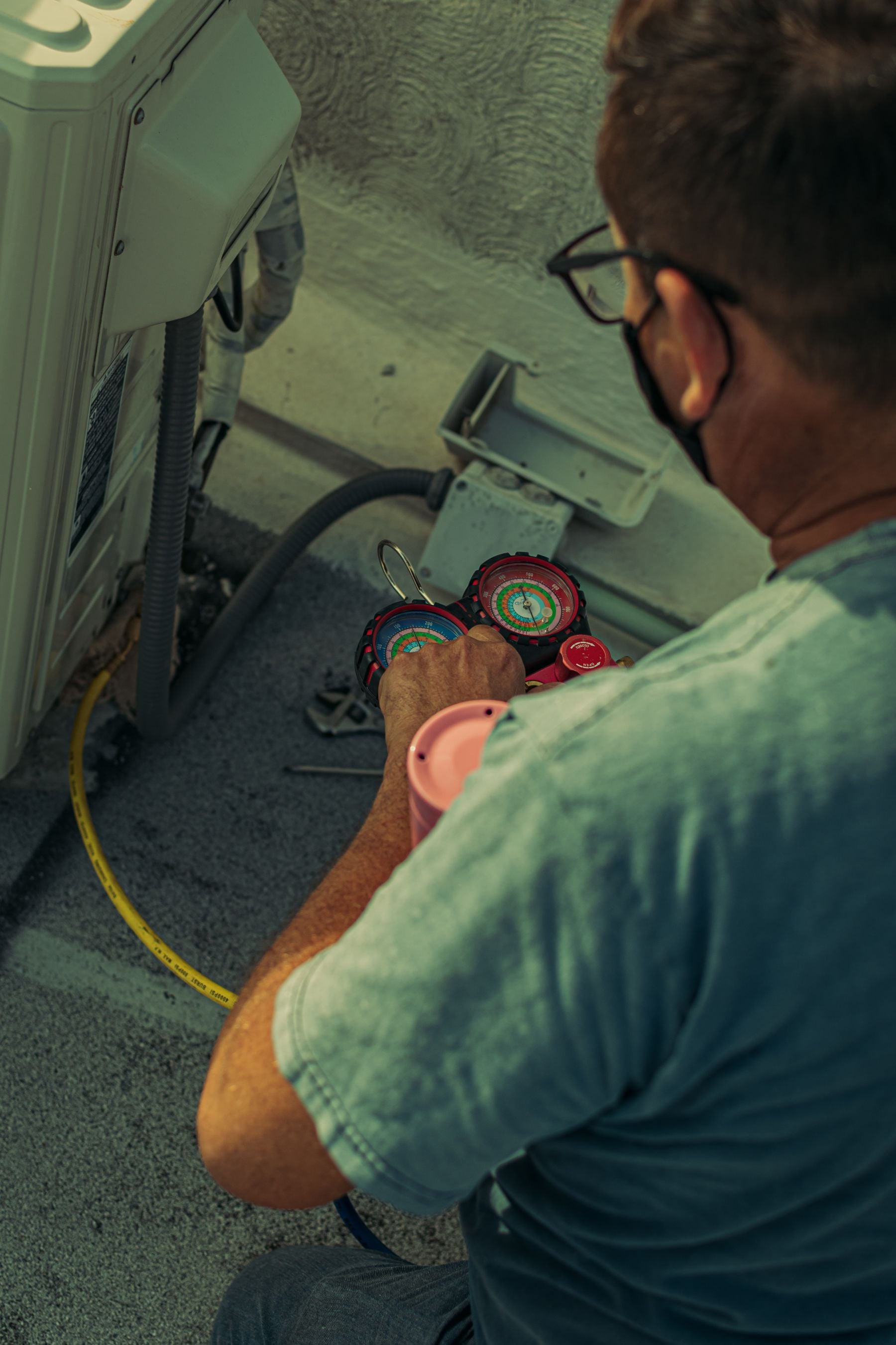 Hands reading a manifold gauge set beside an outdoor unit