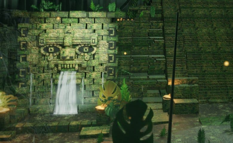 Close view of a stone wall with a large carved face, water pouring from its mouth into a basin, and a stepped temple stair to the right.